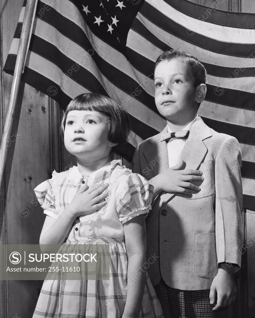Close-up of a boy and a girl taking a Pledge of Allegiance in front of an American flag