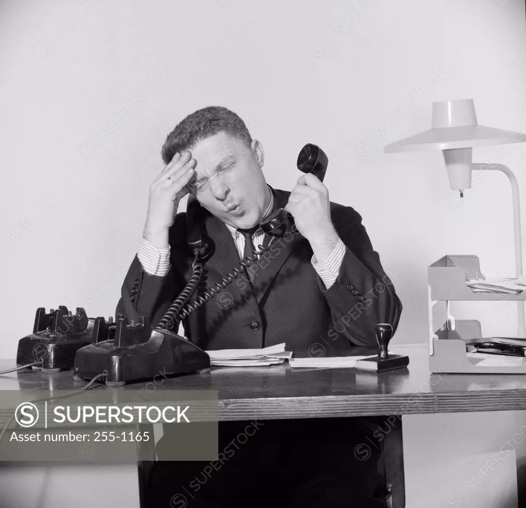 Close-up of a businessman suffering from a headache and using two telephones