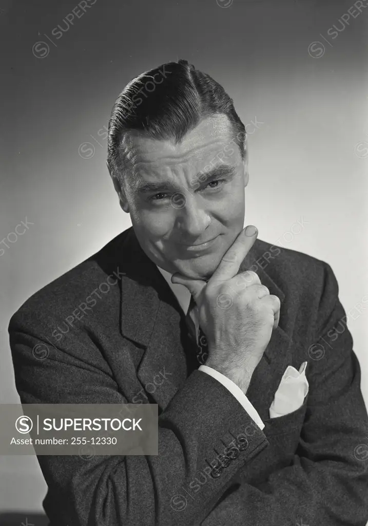 Vintage photograph. Man in suit and tie smirking with hand on chin