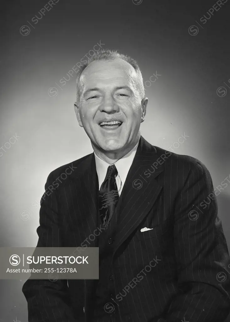Older man in pinstriped dark suit and tie smiling