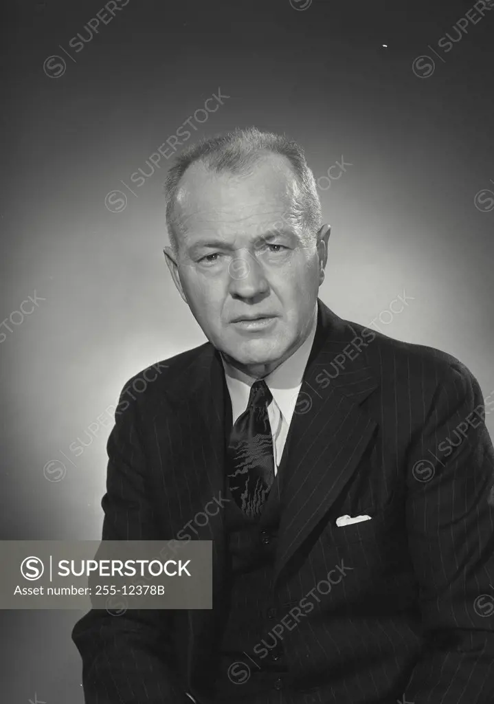Older man in pinstriped dark suit with serious expression on face