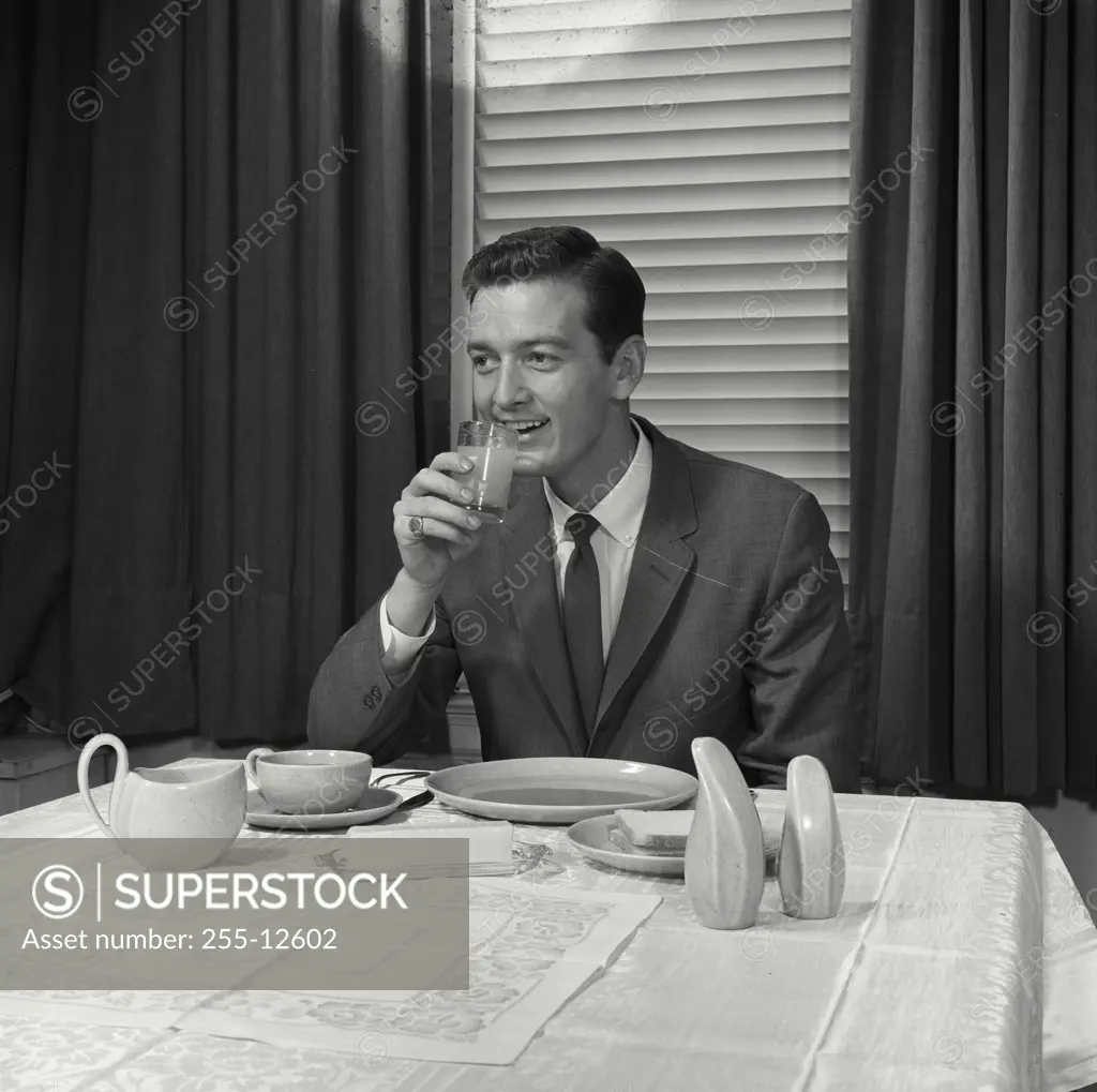 Vintage Photograph. Man in suit sitting at table drinking from glass. Frame 1