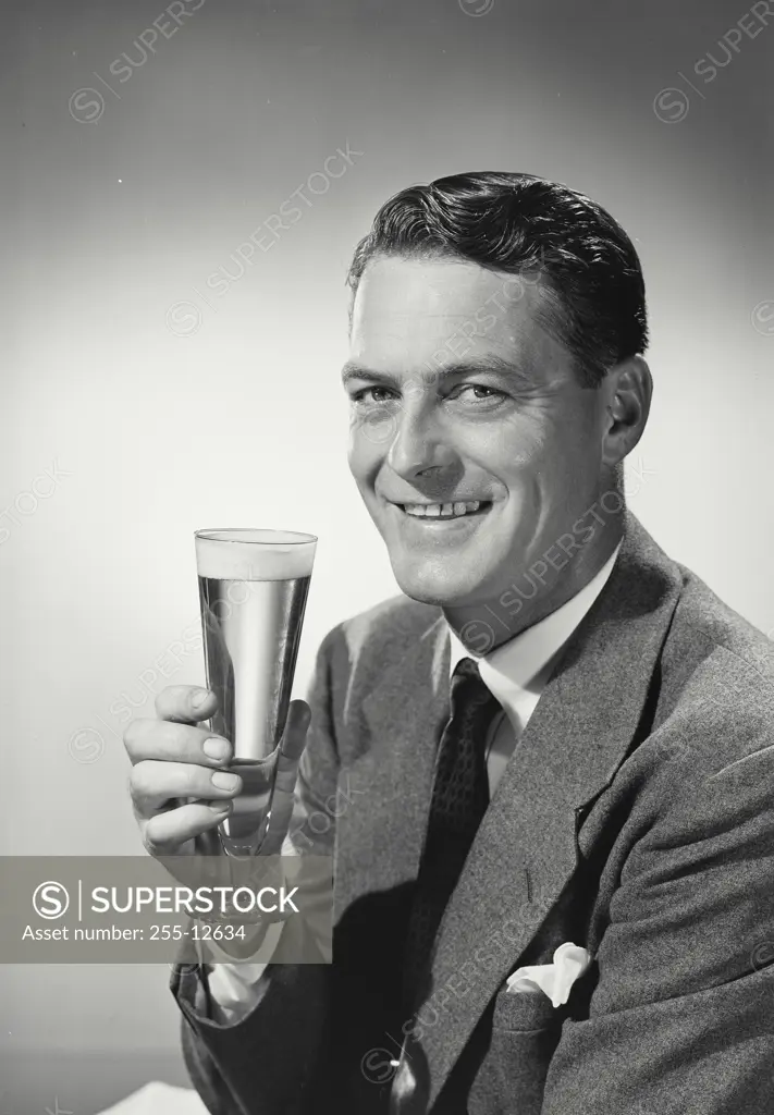 Man in suit and tie holding up glass of beer