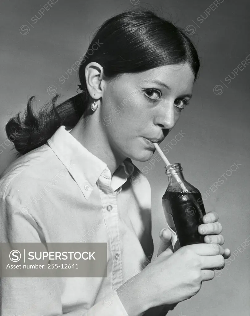 Portrait of a young woman drinking out of a bottle with a drinking straw