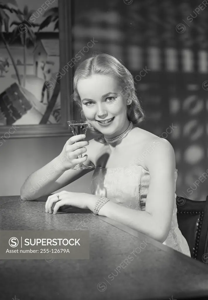 Vintage Photograph. Young woman in dress sitting at bar holding a martini