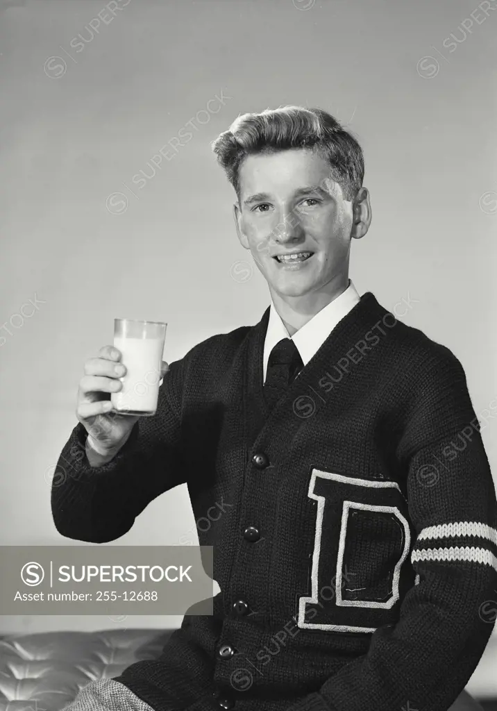 Vintage Photograph. Young man wearing school sweater holding up glass of milk