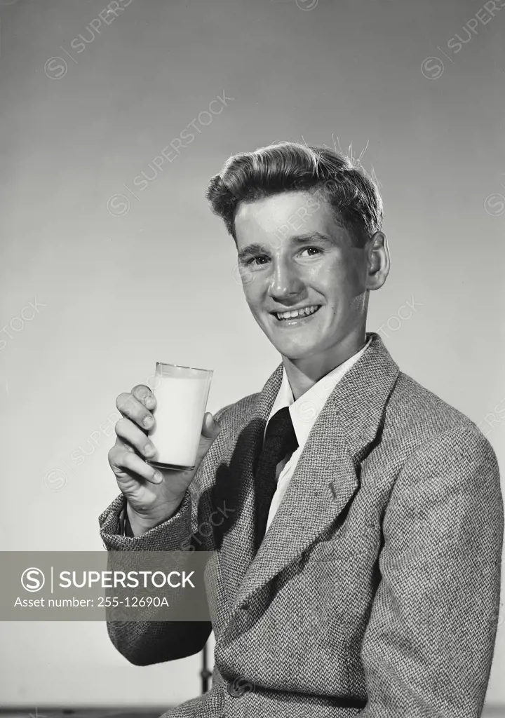 Vintage Photograph. Young man wearing blazer and tie holding up glass of milk