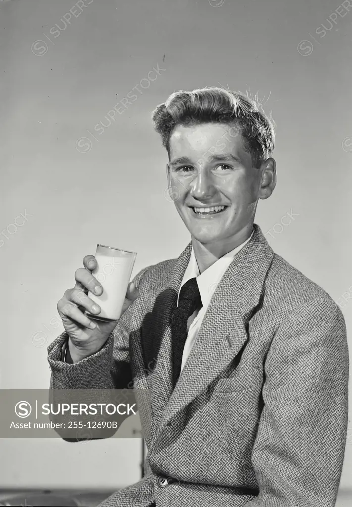 Vintage Photograph. Young man in blazer and tie smiling while holding up glass of milk