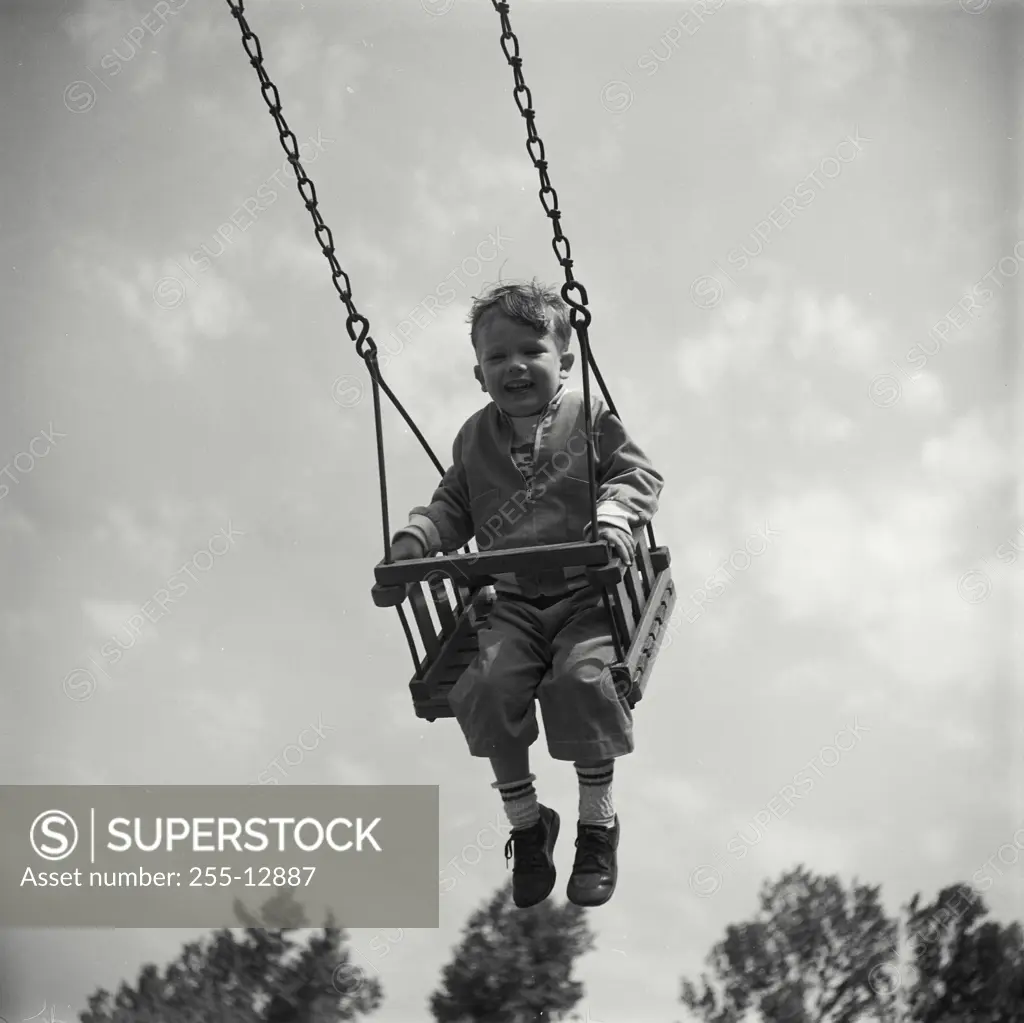 Vintage Photograph. Low angle view of a boy swinging on a swing