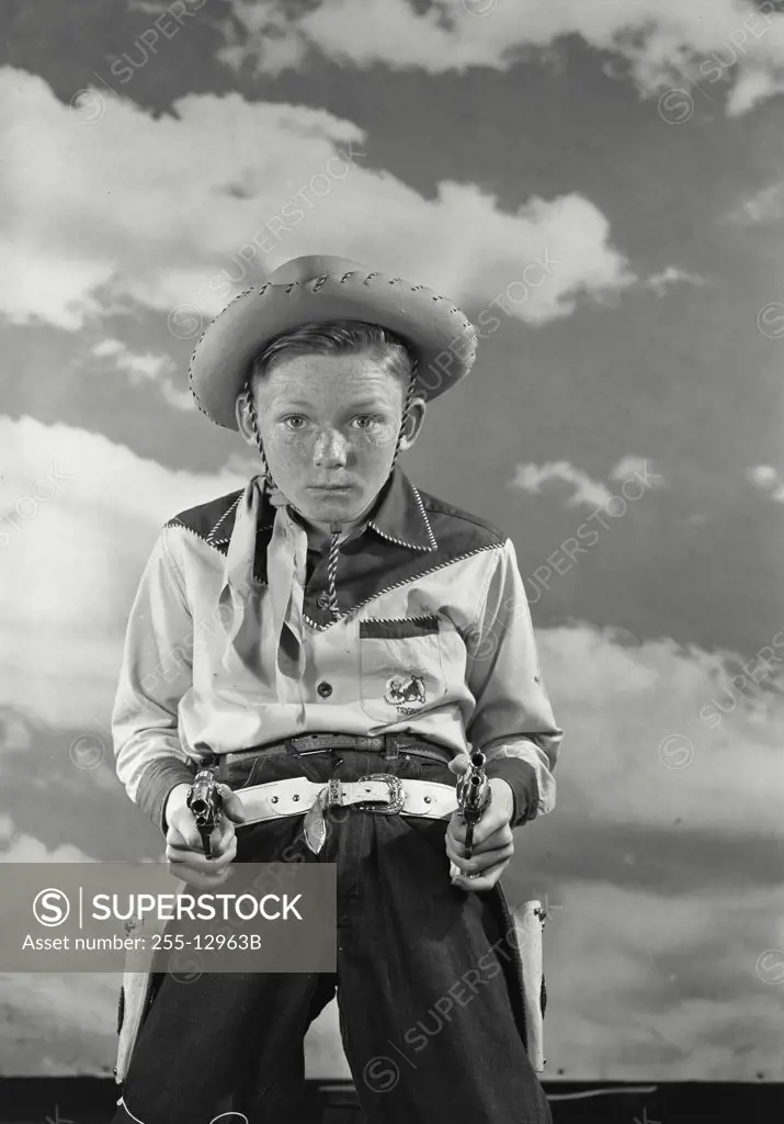 Vintage photograph. Young boy in cowboy costume holding up two toy guns