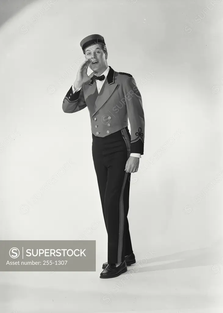 Vintage Photograph. Man wearing bellman uniform standing on white background calling out with right hand near mouth
