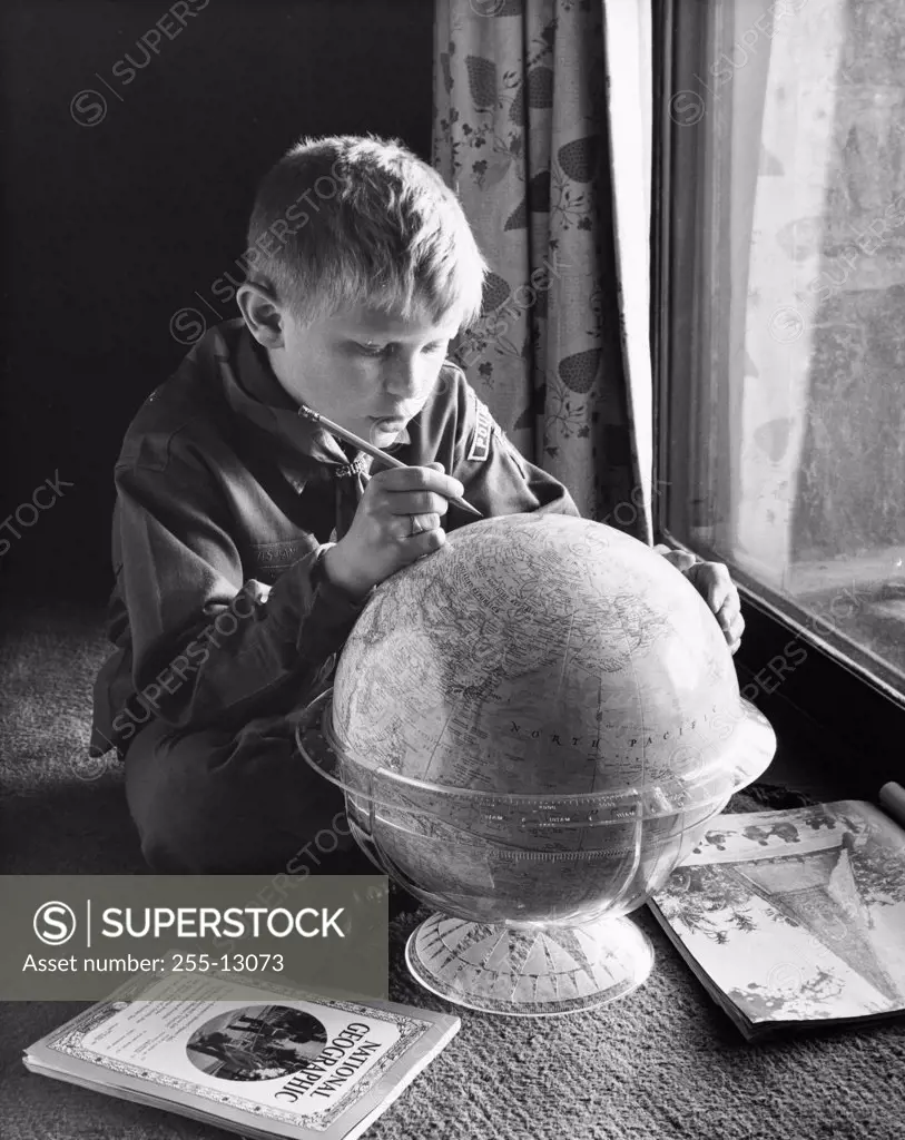 Close-up of a boy holding a pencil and marking on a globe