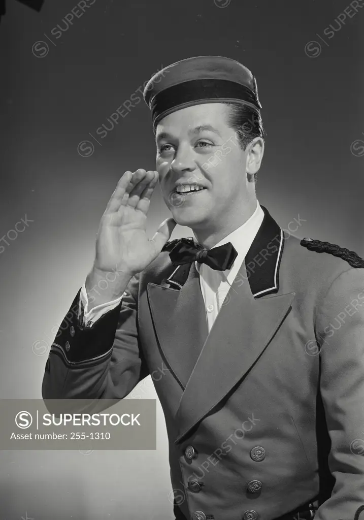 Vintage Photograph. Smiling bellman calling out with cupped hand raised near mouth