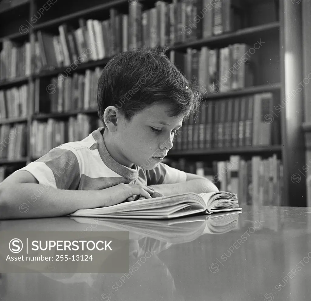 Vintage Photograph. Young boy in library reading book at table.