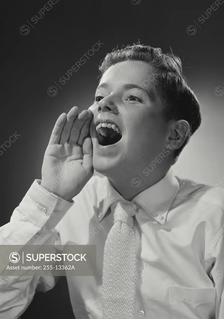 Vintage Photograph. Boy wearing white dress shirt and tie holding hand up near mouth calling out