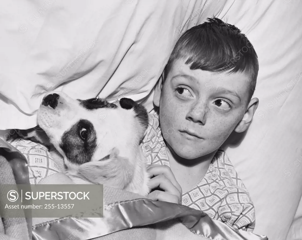 Close-up of a boy lying with his puppy on a bed