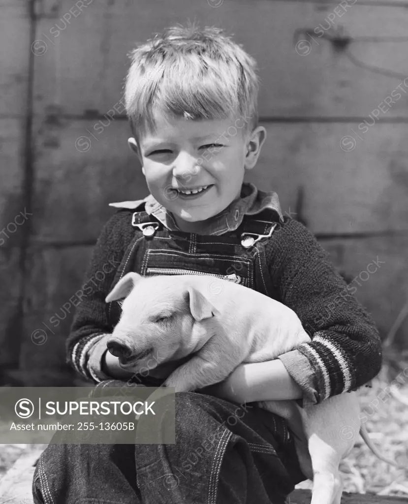 Close-up of a boy holding a piglet and smiling
