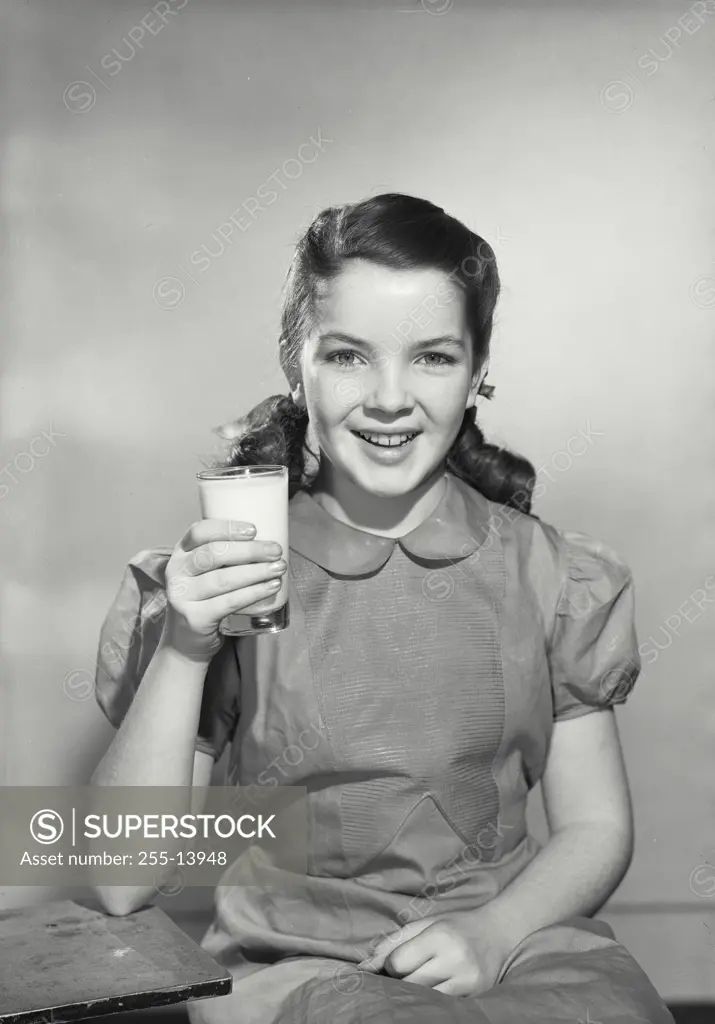 Vintage Photograph. Young smiling brunette girl wearing dress holding up glass of milk