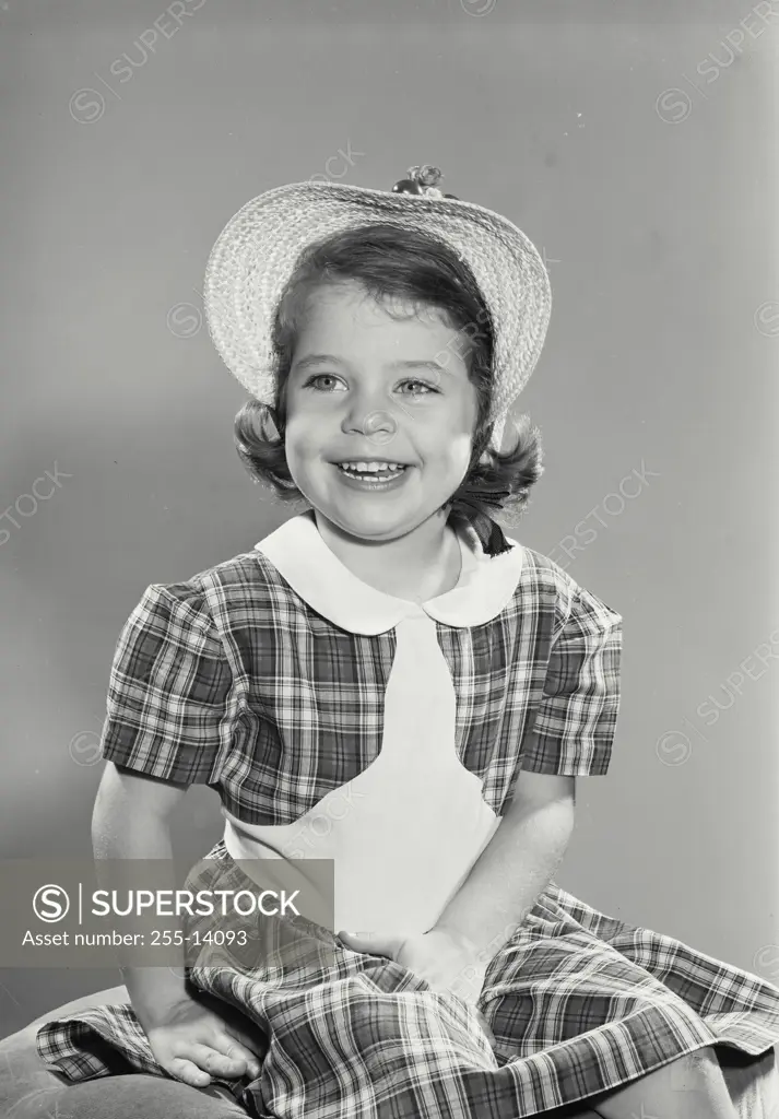Vintage Photograph. Young girl in plaid dress and hat sitting and smiling