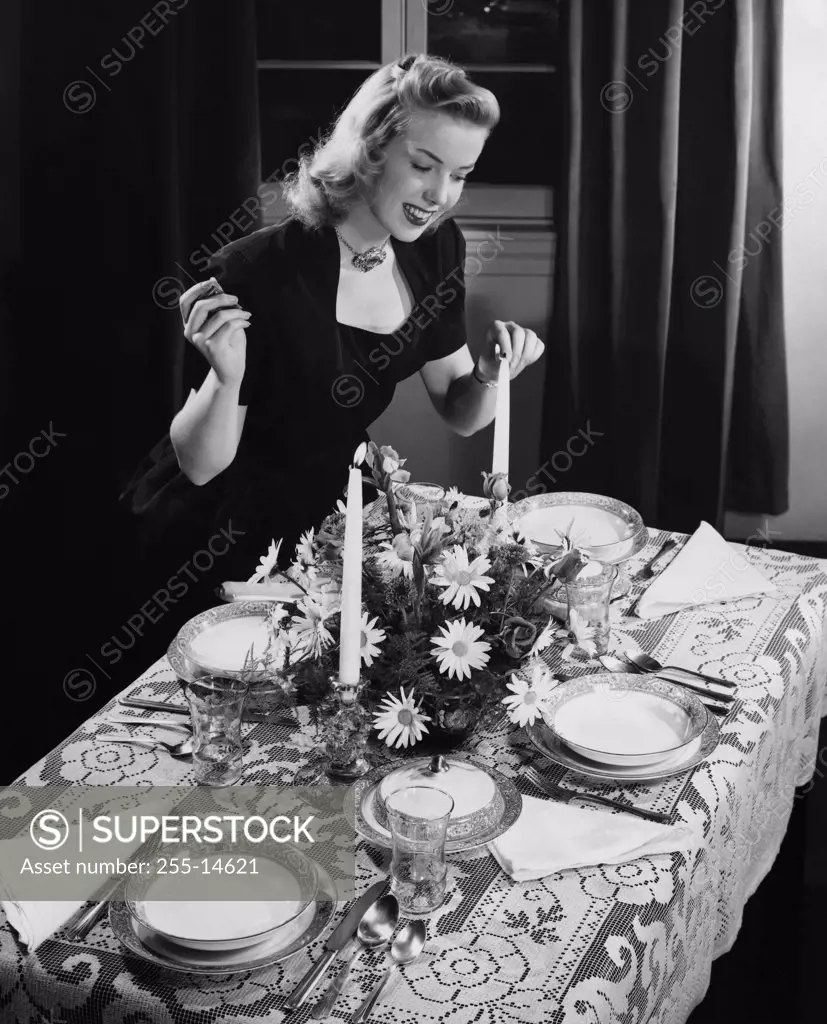 High angle view of a young woman lighting a candle on a dining table