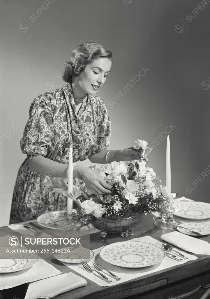Woman putting flowers in centerpiece at dinner table.