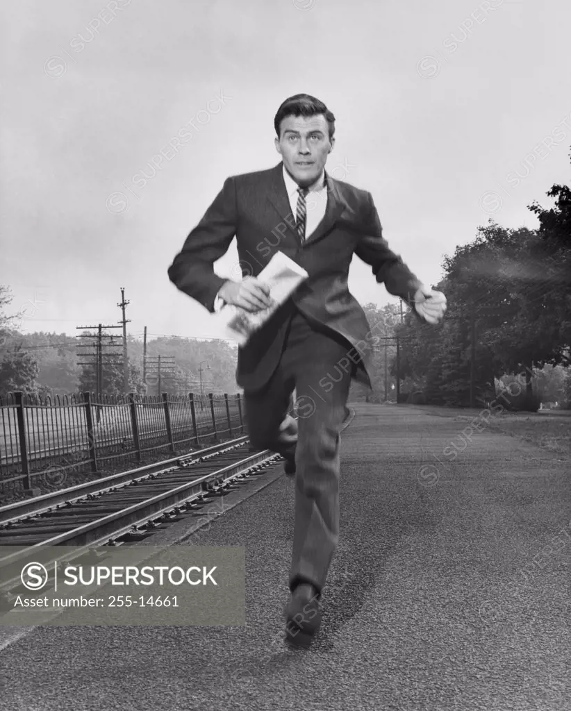 Businessman running along a railroad track carrying a newspaper
