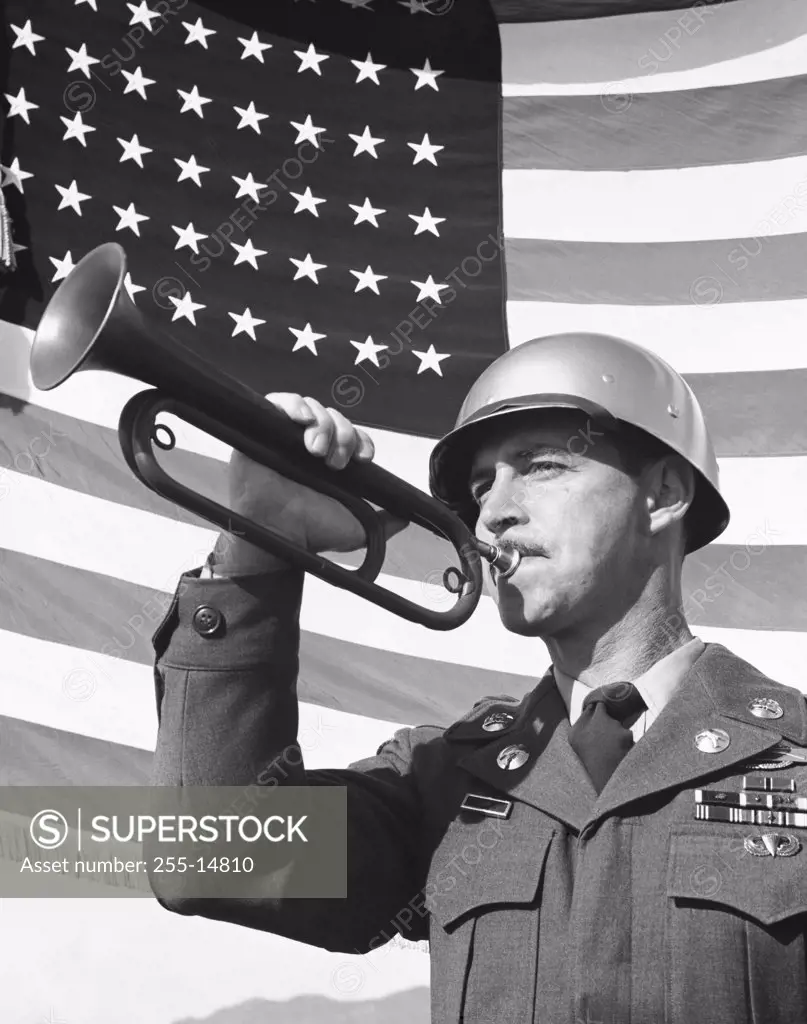Low angle view of an army soldier blowing a bugle in front of the American flag