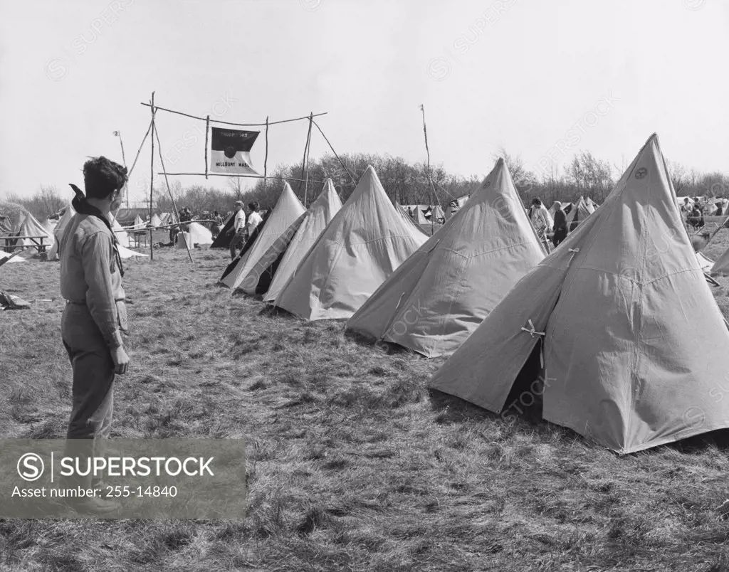 Side profile of a boy scout standing near tents