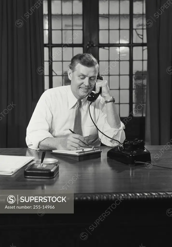 Vintage Photograph. Man in btton shirt and tie sitting at desk on telephone.