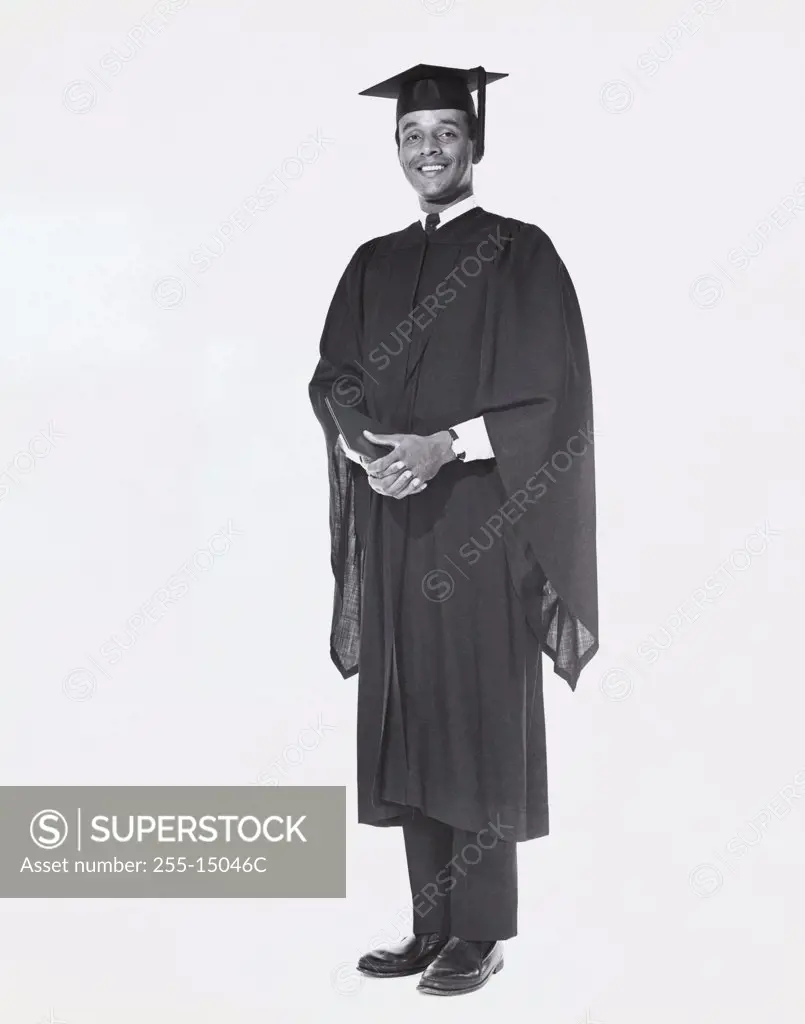 Young man wearing a graduation gown and holding a book