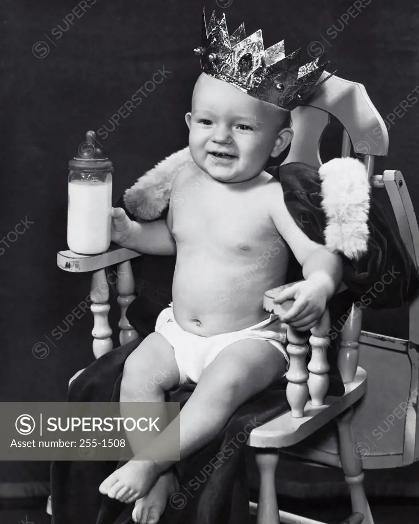 Close-up of a baby boy wearing a crown sitting in an armchair