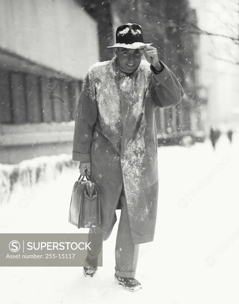 Vintage Photograph. Man in long coat with briefcase tipping hat while walking through snow