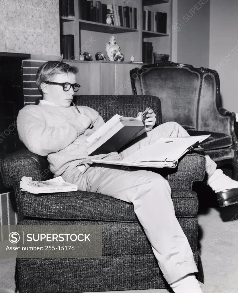 Teenage boy reading a book in an armchair