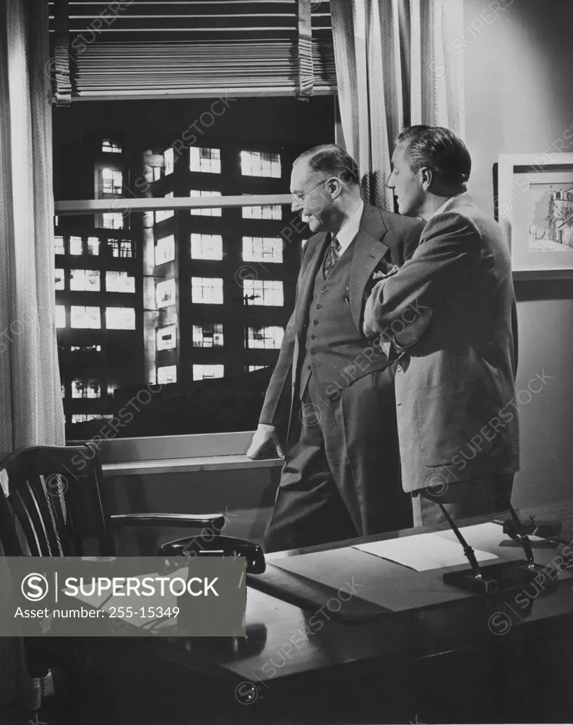 Two businessmen in office looking through window, 1950s