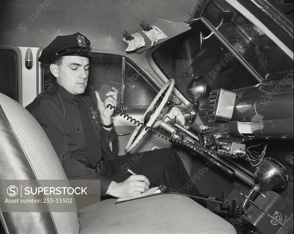 Vintage photograph. Police officer sitting in a police car getting call by CB radio from Headquarters.