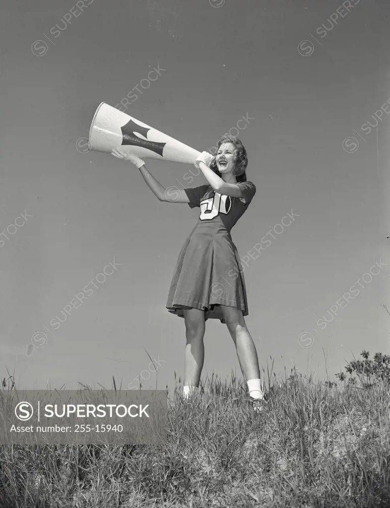 Vintage photograph. Low angle view of a female cheerleader shouting into a megaphone