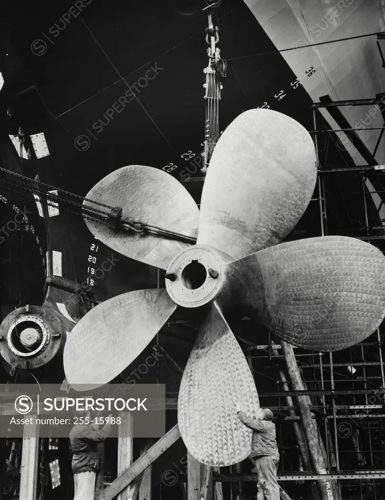 Vintage Photograph. Two mature men working on the propeller of an industrial ship