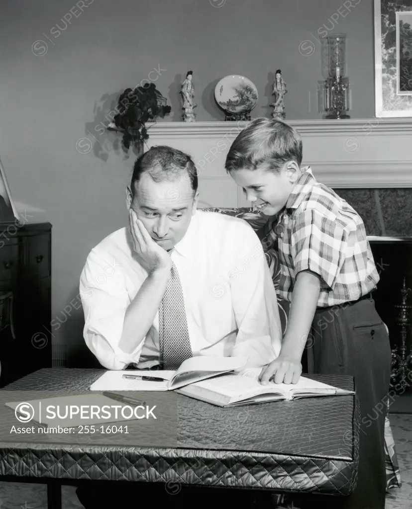Father sitting in front of a book with his son standing beside him smiling