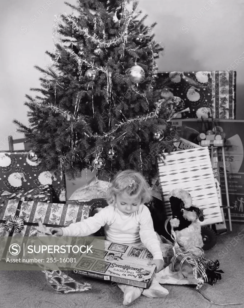 Girl sitting in front of a Christmas tree and opening a Christmas present