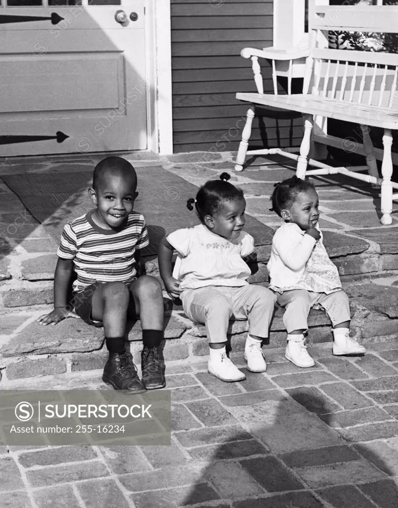 Two girls and a boy sitting on a step on the porch