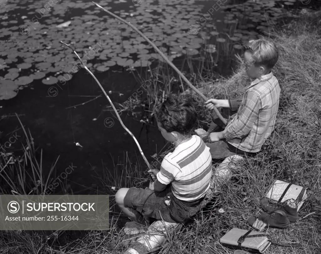 Two boys sitting and fishing with homemade fishing rod