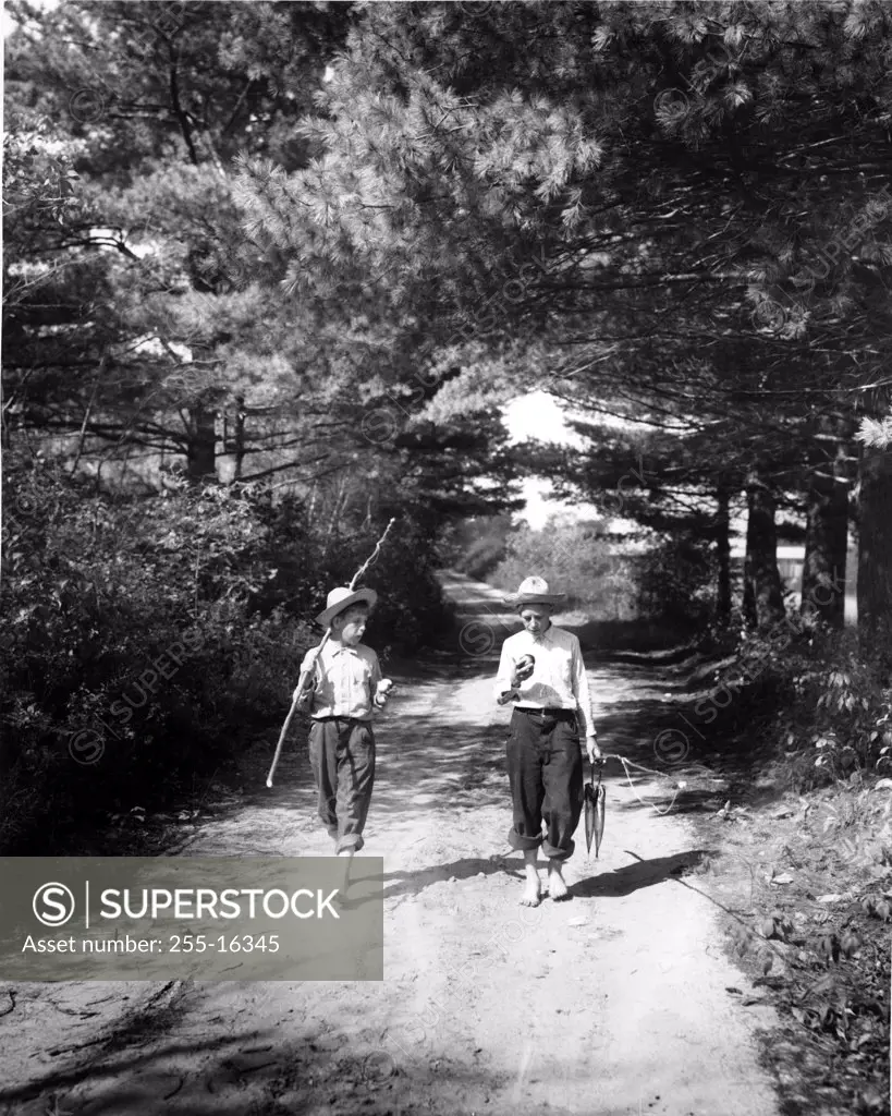 Vintage photograph of boys on forest footpath carrying improvised fishing rod and catch of fish