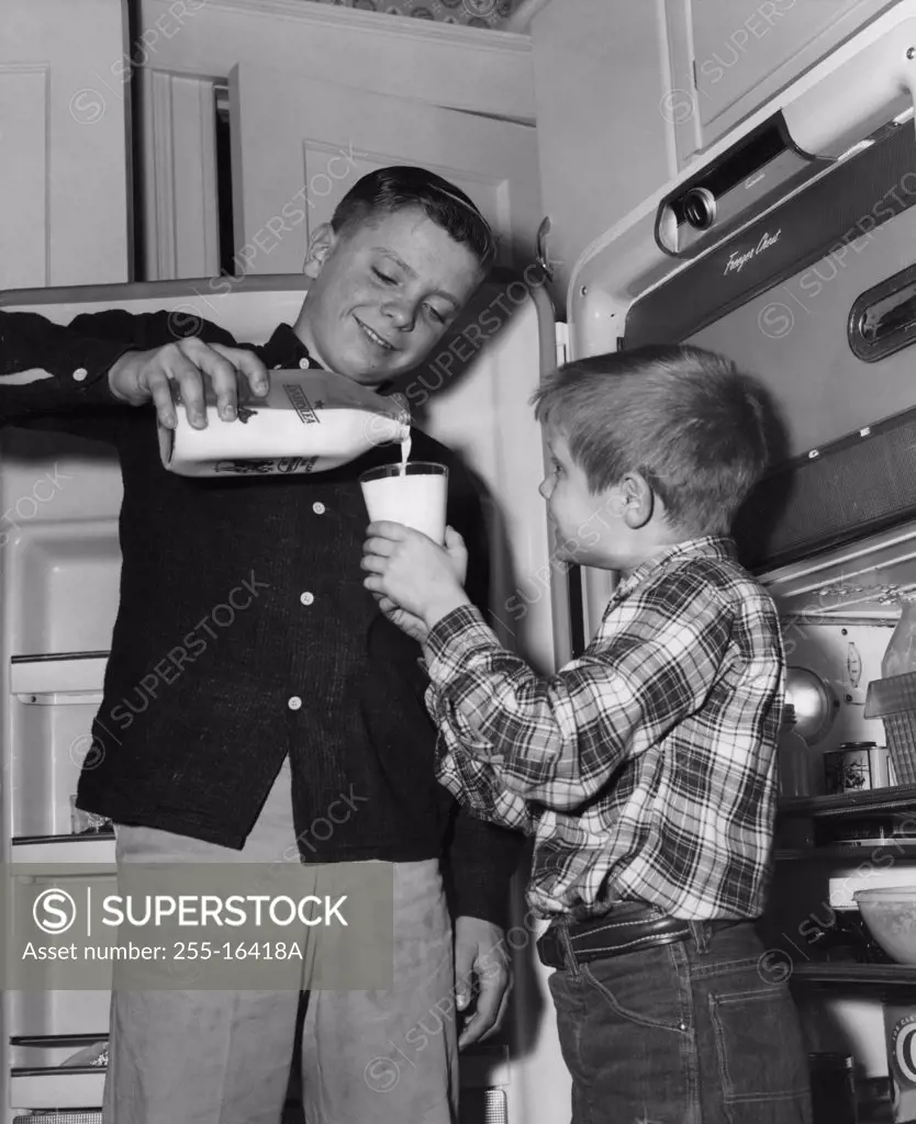 Older brother pouring milk from bottle into glass of younger brother