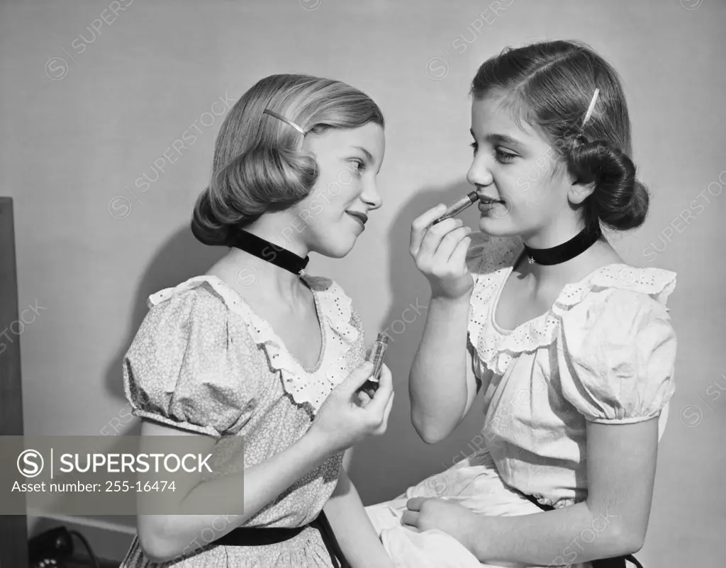 Side profile of two girls applying lipstick
