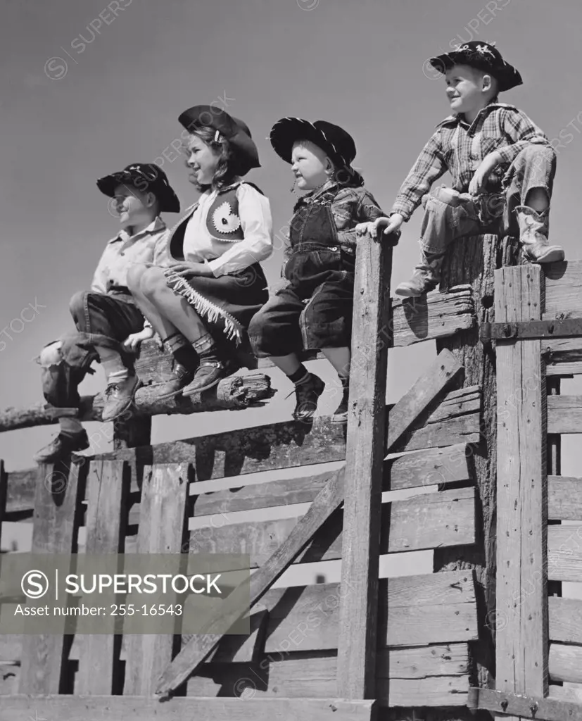 Four children dressed as cowboys and sitting on a wooden fence