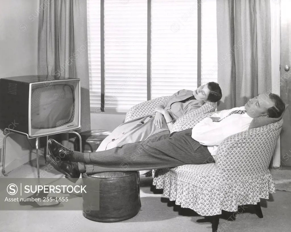 Mid adult couple sleeping in chairs in front of a television