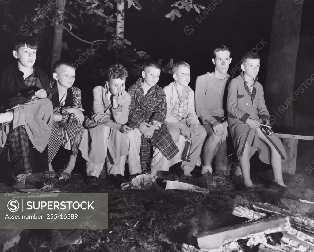 Group of boys sitting side by side in front of a campfire