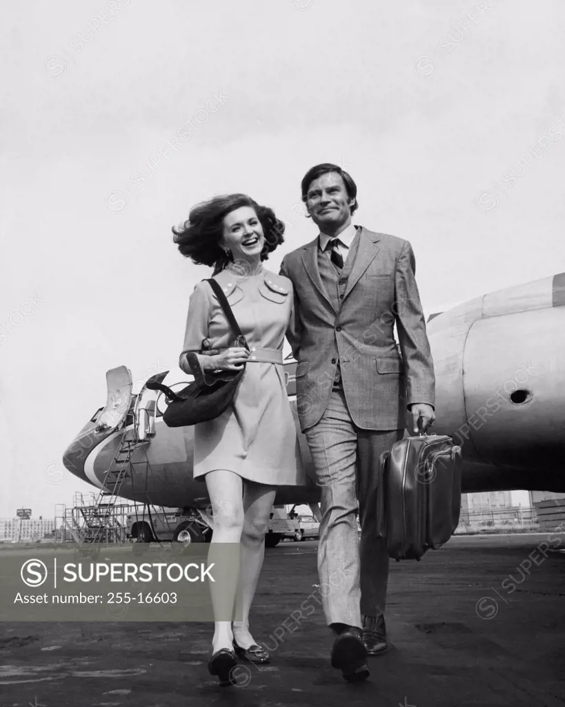 Businessman with a businesswoman walking near an airplane and smiling