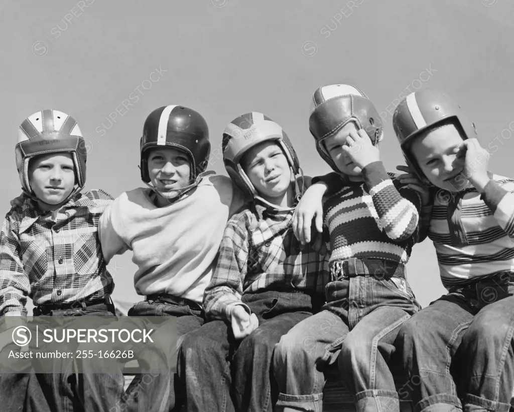 Five boys wearing sports helmets and sitting together