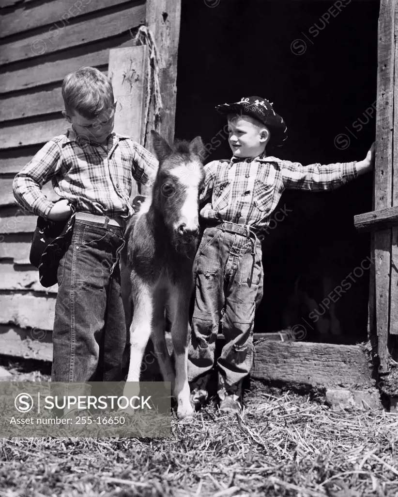 Two cowboys standing with a foal in front a stable